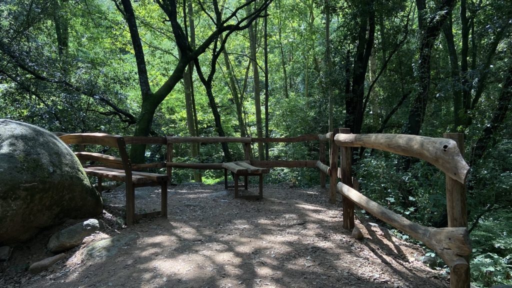 Foto: Tourdera. Zona de descans amb baranes i bancs al passeig per la riera d'Arbúcies